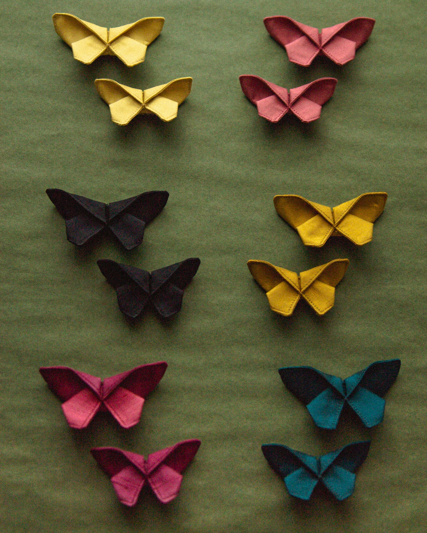 All the different colors of the small Origami Silk Butterfly Hair Clips on green background.